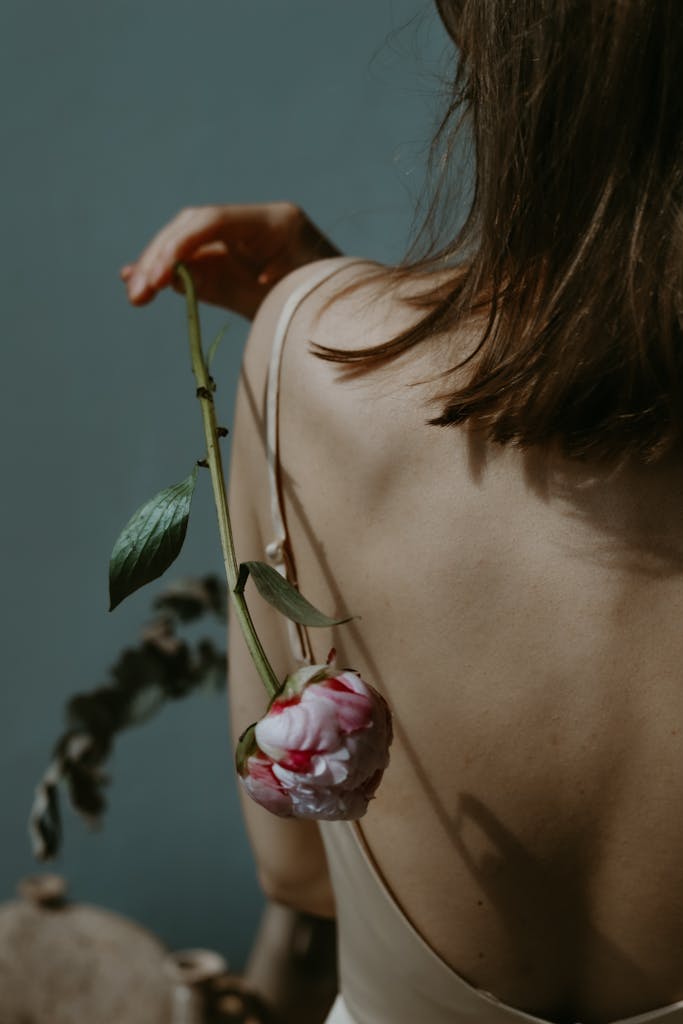 An artistic image of a woman with a peony flower against her bare back, conveying elegance.